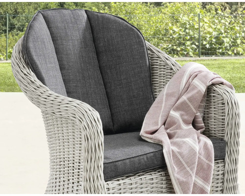 Gartensessel aus Polyrattan mit dunklen Sitz- und Rückenkissen sowie einer gestreiften Decke im Garten.