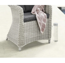 Geflochtener Gartenstuhl im Rattan-Stil mit Sitzkissen, einer gestreiften Decke und einer Trinkflasche in einem hellen Außenbereich.