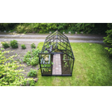 Freistehendes Gewächshaus aus Glas mit schwarzem Rahmen und Satteldach in einem Garten mit Pflanzen und gepflastertem Weg.