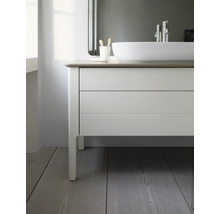 Moderner Badunterschrank mit hellen Fronten, zwei Auszügen und Aufsatzwaschbecken auf einem Holzfußboden in einem hellen Badezimmer.