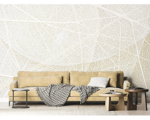 Fototapete mit filigranem Blattstruktur-Motiv in einem hellen Wohnzimmer hinter einem Sofa mit Kissen und Beistelltischen.