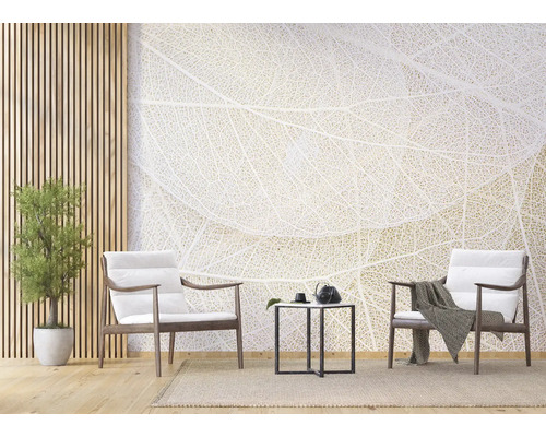 Helles Wohnzimmer mit Fototapete im Blattadern-Design, zwei Holzsesseln mit weißen Polstern, schwarzem Beistelltisch und Zimmerpflanze.