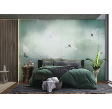 Fototapete im Schlafzimmer mit weißen Kranichen im nebligen Wald, grünes Bett mit Kissen, Holzpaneele an der Wand und Zimmerpflanze.