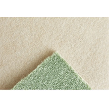 Grüner Teppichboden mit strukturierter Oberfläche und beigem Filzrücken. Detailaufnahme der Materialstruktur.
