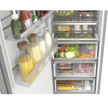 Gut organisierter, offener Kühlschrank mit Obst, Gemüse, Fleisch und Getränken in verschiedenen Frischefächern und Türabstellern.
