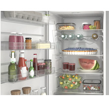 Offener, organisierter Kühlschrank mit Glasablagen, gefüllt mit frischen Lebensmitteln wie Salat, Obst, Säften und Saucen.