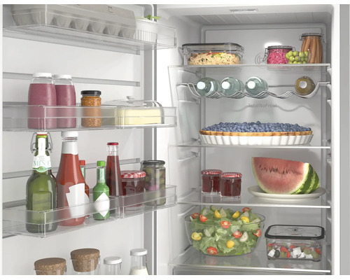 Offener, organisierter Kühlschrank mit Glasablagen, gefüllt mit frischen Lebensmitteln wie Salat, Obst, Säften und Saucen.