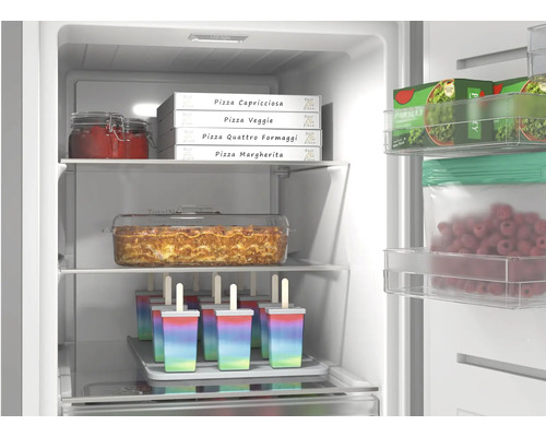 Gut organisierter Gefrierschrank mit Pizzakartons, Lasagneform und Eis am Stiel. Helle Innenbeleuchtung und Glasablagen.