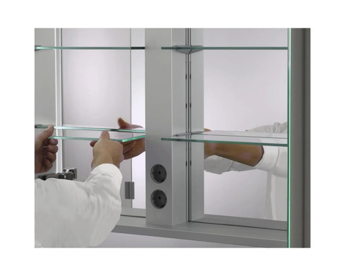 Innenansicht eines Spiegelschranks mit Glaseinlegeböden und zwei integrierten Steckdosen, Hände setzen einen Glasboden ein.
