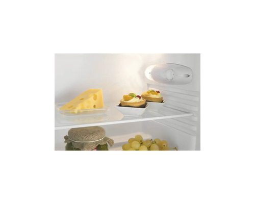 Innenansicht eines Kühlschranks mit Glasablagen, Käse, Törtchen und Weintrauben. Helle Beleuchtung und Temperaturregler sind sichtbar.