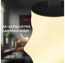 Nahaufnahme eines dreidimensional gedruckten Lampenschirms mit Wellenstruktur und warmem Licht vor einem Wohnzimmerhintergrund.