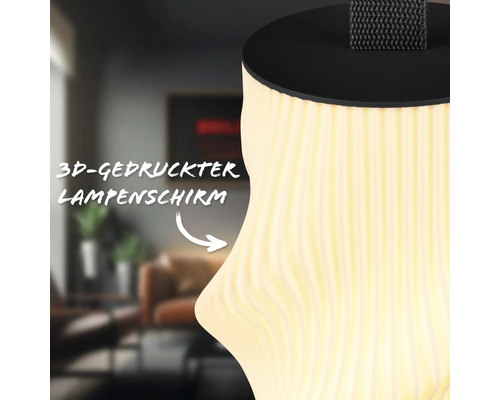Nahaufnahme eines dreidimensional gedruckten Lampenschirms mit Wellenstruktur und warmem Licht vor einem Wohnzimmerhintergrund.