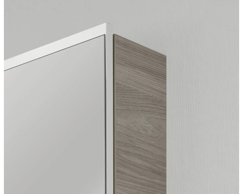 Nahaufnahme der Ecke eines Spiegelschranks mit weißem Rahmen und Seitenwand in Holzoptik.