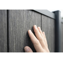 Eine Hand berührt die strukturierte Oberfläche eines Zaunpaneels in Holzoptik aus Holz-Kunststoff-Verbundwerkstoff.