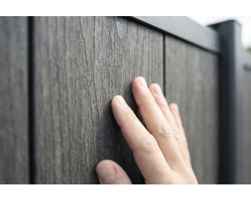 Eine Hand berührt die strukturierte Oberfläche eines Zaunpaneels in Holzoptik aus Holz-Kunststoff-Verbundwerkstoff.