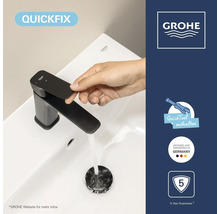 Hand bedient schwarze Grohe Waschtischarmatur auf weißem Becken. Symbole: QuickFix, Werkzeug, deutsches Design, fünf Jahre Garantie. Grohe Logo.
