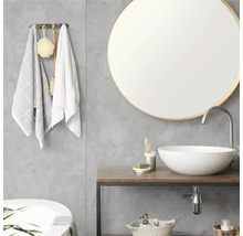 Modernes Badezimmer mit rundem Spiegel, weißer Waschschale auf einem Waschtisch in Holzoptik und grauer Wand in Betonoptik.