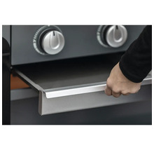 Eine Hand zieht die Fettauffangschale unter den Drehreglern eines Gasgrills heraus.