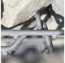 Nahaufnahme eines Gabionendrahtgeflechts mit Steinen. Fokus auf die ineinandergreifenden Metalldrähte und Haken des verzinkten Stahlkorbs.