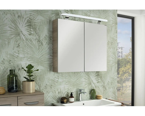Moderner Spiegelschrank mit zwei Türen und LED-Beleuchtung über einem Waschbecken in einem hellen Badezimmer mit gemusterter Tapete.