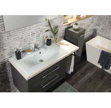 Modernes Badezimmer mit dunkelgrauem Waschtisch, Glaswaschbecken und quadratischer Badewanne vor Wänden in Steinoptik.