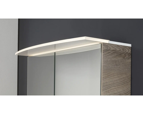 Spiegelschrank mit LED-Aufsatzleuchte und Korpus in Holzoptik.