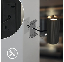 Technische Zeichnung der Montage einer zylindrischen Wandleuchte mit Wandhalterung, Schrauben, Kabel und Montagesymbol.
