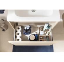 Geöffnete Schublade eines hellen Waschtischunterschranks mit Badutensilien wie Toilettenpapier und Pflegeprodukten unter einem weißen Waschbecken.