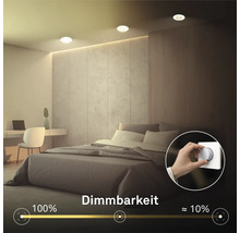 Schlafzimmer mit Einbaustrahlern an der Decke und einer Hand, die einen Drehdimmer an der Wand betätigt, zur Veranschaulichung der Dimmbarkeit.