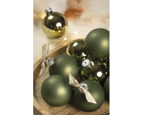 Grüne Weihnachtskugeln in matten und glänzenden Ausführungen mit silbernen Kappen und dekorativen Schleifen auf einem Holztablett.
