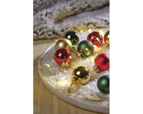 Festliches Arrangement aus Weihnachtsbaumkugeln in Rot, Grün und Gold auf einem Tablett mit Kunstschnee und LED-Lichterkette.