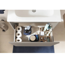 Draufsicht auf eine geöffnete Schublade eines Waschtischunterschranks mit Toilettenpapier, Kosmetik und Organizer für Badutensilien.