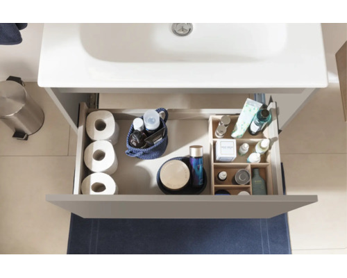 Draufsicht auf eine geöffnete Schublade eines Waschtischunterschranks mit Toilettenpapier, Kosmetik und Organizer für Badutensilien.