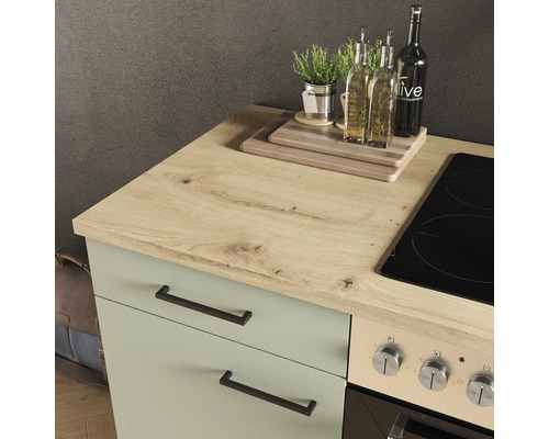 Küchenarbeitsplatte in Eichenoptik auf einem grünen Unterschrank neben einem Glaskeramikkochfeld und Backofen.