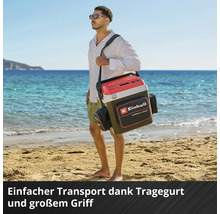 Einhell Kühlbox mit Tragegurt, großem Griff und Zubehörtasche, getragen von einem Mann an einem hellen Sandstrand.