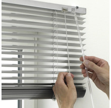 Nahaufnahme einer Hand, die eine silberne Aluminium-Jalousie mit transparentem Wendestab und Zugschnur bedient.