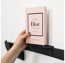 Eine Hand platziert ein Buch auf einem minimalistischen, schwarzen Wandregal aus Metall an einer Wand.