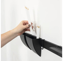 Hand legt einen Stift in einen an einer Wandleiste befestigten Aufbewahrungsbecher zur Organisation von Schreibwaren oder Werkzeugen.