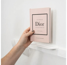 Eine Hand platziert das Buch Little Book of Dior auf einem schmalen weißen Wandregal.