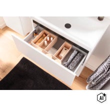 Geöffnete Schublade eines weißen Waschbeckenunterschranks mit hölzernen Ordnungsboxen für Kosmetik. (Image AI modified or generated)