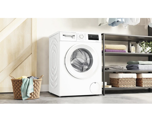 Bosch Waschmaschine in einem hellen Waschraum neben einem Regal mit Handtüchern und einem Wäschekorb.