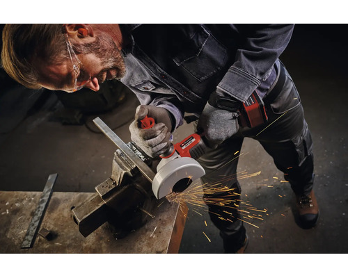 Handwerker mit Schutzbrille nutzt Einhell Akku Winkelschleifer zum Trennen von Metall in einem Schraubstock mit Funkenflug in der Werkstatt