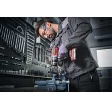 Handwerker bohrt mit einem Akku-Bohrschrauber ein Metallstück in einer Werkstatt mit organisierter Werkzeugwand.