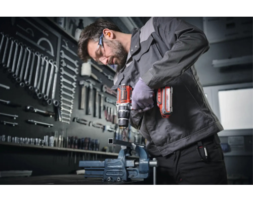 Handwerker bohrt mit einem Akku-Bohrschrauber ein Metallstück in einer Werkstatt mit organisierter Werkzeugwand.