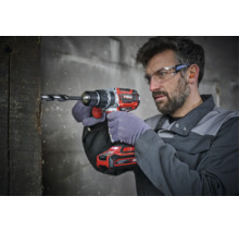 Handwerker mit Schutzbrille bohrt mit einem Akku-Bohrschrauber der Marke Einhell in einen Holzbalken.