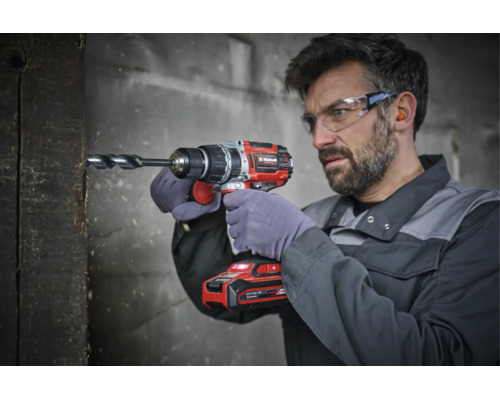 Handwerker mit Schutzbrille bohrt mit einem Akku-Bohrschrauber der Marke Einhell in einen Holzbalken.