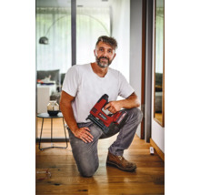 Handwerker kniet auf einem Holzboden und hält einen Akku Tacker der Marke Einhell in der Hand in einem modernen Wohnraum.