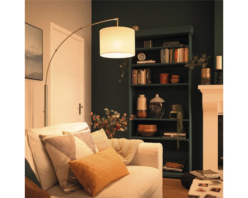 Moderne Bogenlampe mit Stoffschirm neben einem hellen Sofa in einem gemütlich eingerichteten Wohnzimmer mit dunklem Bücherregal.