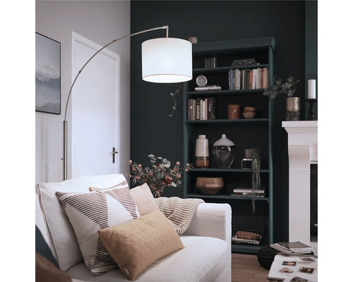 Moderne Bogenlampe mit Stoffschirm neben einem Sofa in einem gemütlichen Wohnzimmer mit dunklem Regal und Kamin.