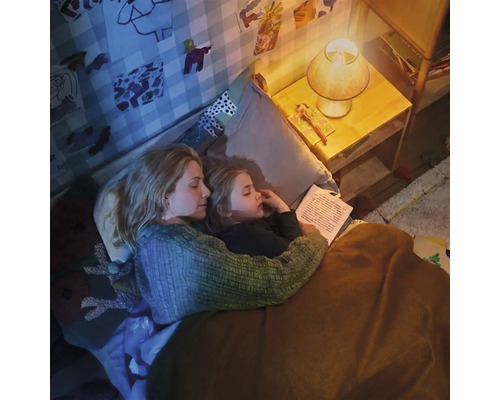 Mutter und Kind lesen abends gemeinsam ein Buch im Kinderzimmer bei gemütlichem Licht der Nachttischlampe.